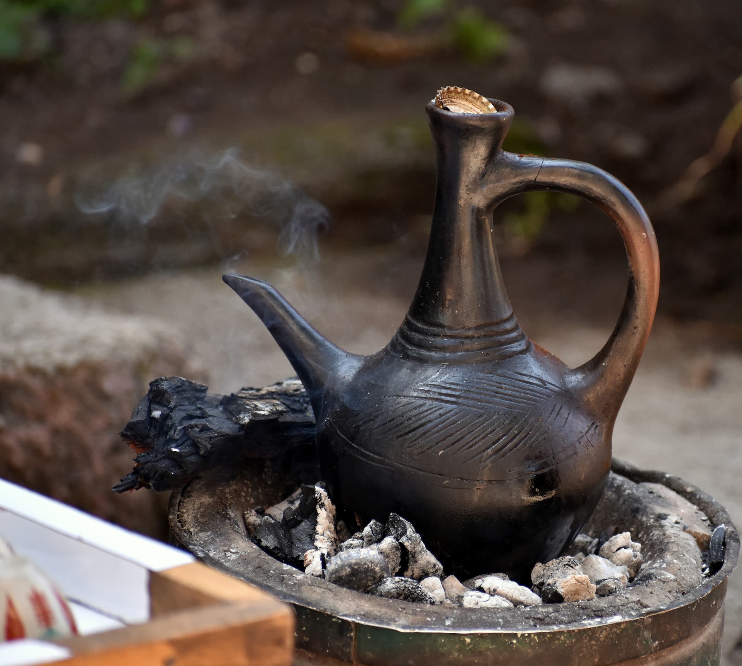 Schwarze traditionelle Kaffeekanne aus Ton, die auf gluehenden Kohlen erhitzt wird.