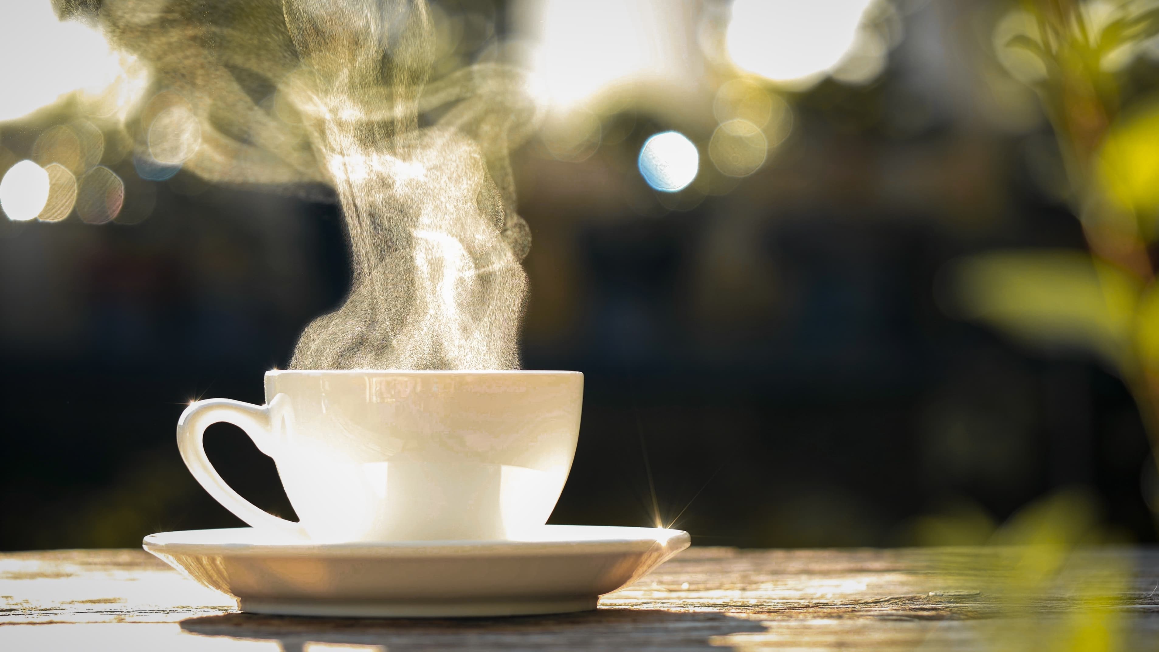 Weiße Tasse mit dampfendem Kaffee auf Holztisch im Freien.