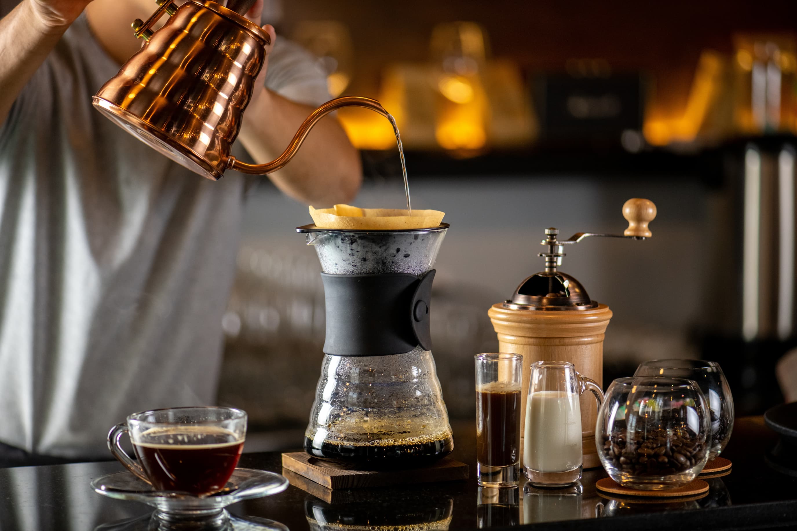 Barista bereitet Pour Over Kaffee mit Handfilter, Wasserkessel und Glaskanne zu.