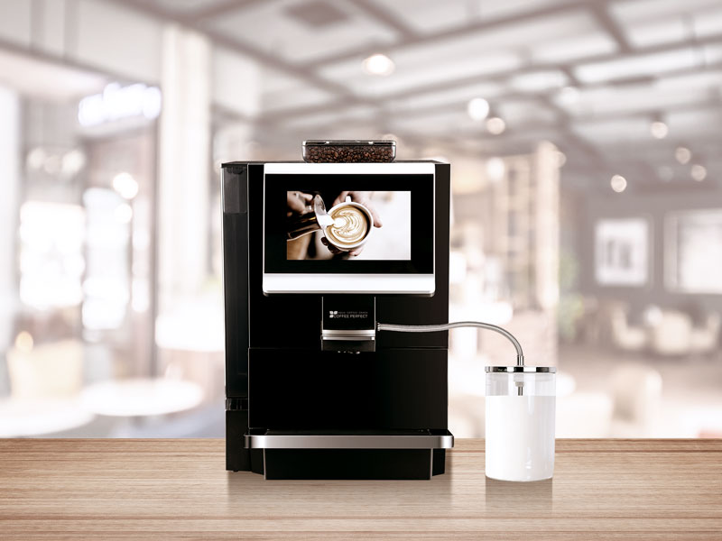 Kaffeevollautomat MP10 mit Milchbehaelter auf Holztresen in modernem Caféambiente, im Hintergrund unscharfer Gastraum.
