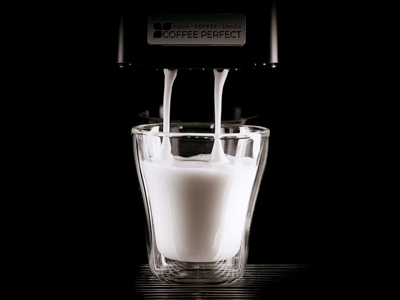 Eine Tasse Milch unter einer laufenden Kaffeemaschine