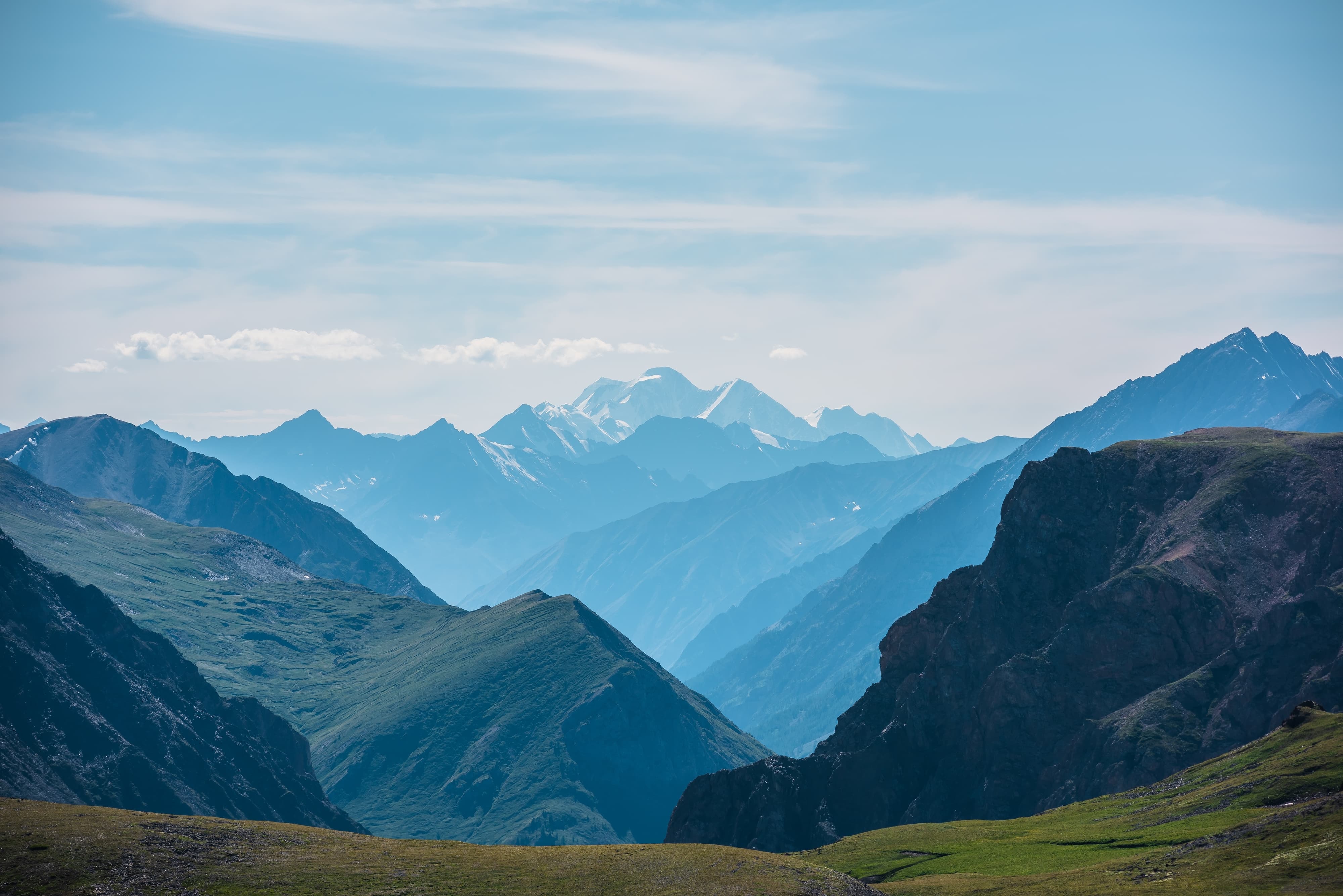 Majestätisches Bergpanorama mit grünen Tälern und verschneiten Gipfeln in der Ferne.