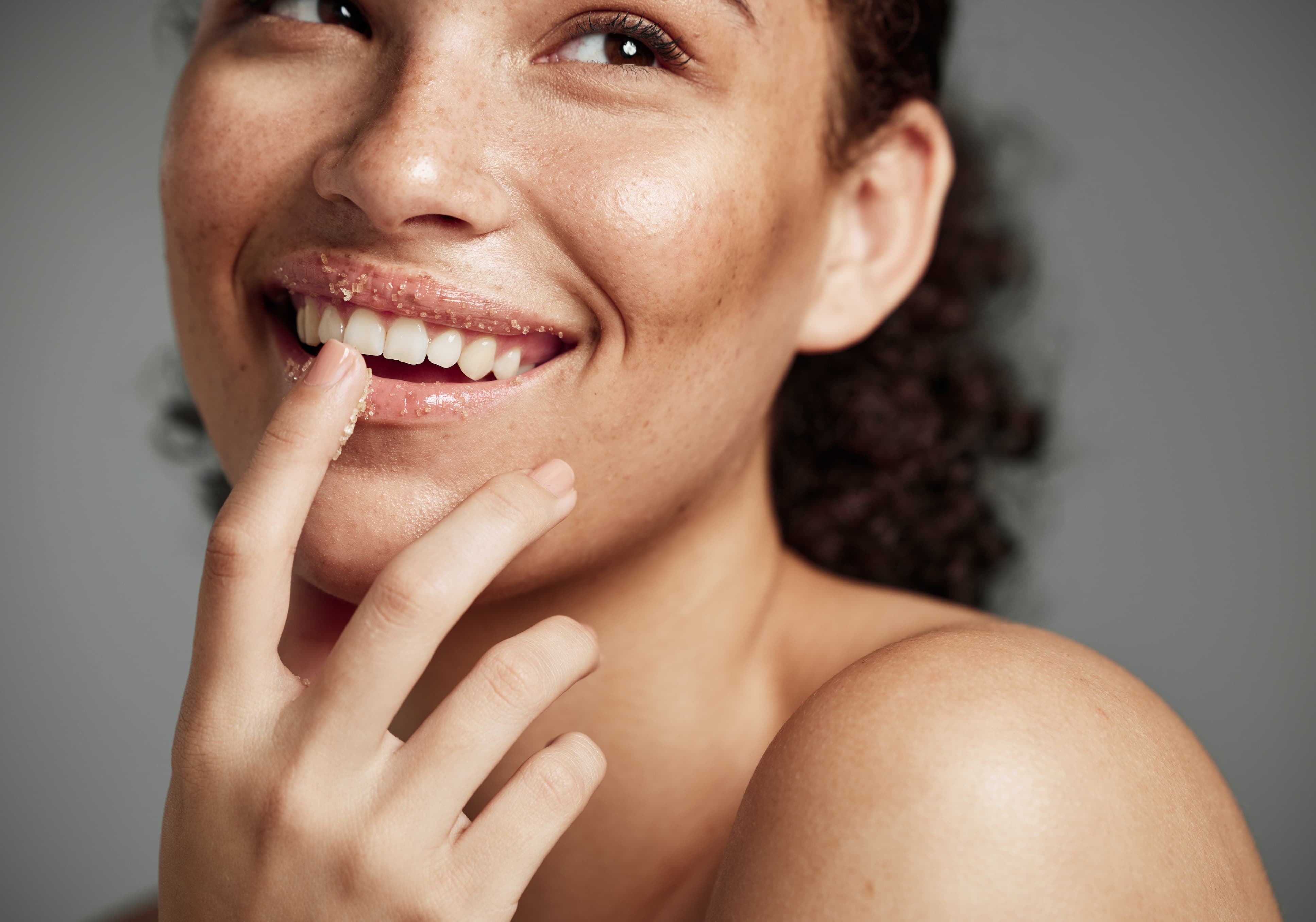 Frau trägt Lippenpeeling mit Kaffeepartikeln auf und lächelt.