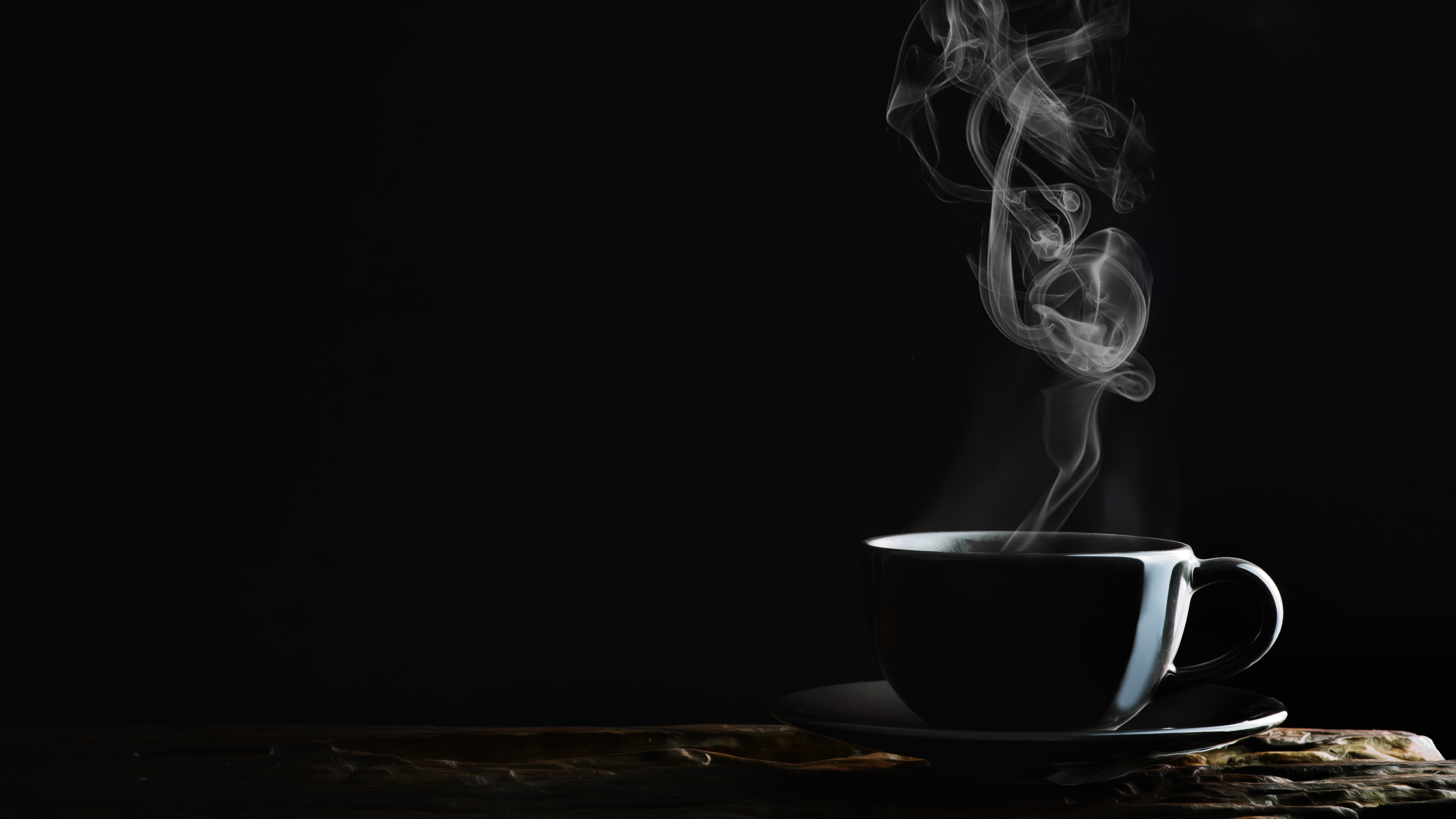 Schwarze Kaffeetasse mit aufsteigendem Dampf auf dunklem Hintergrund.