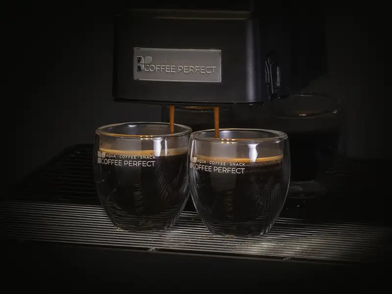 Zwei Tassen Kaffee unter einer laufenden Kaffeemaschine