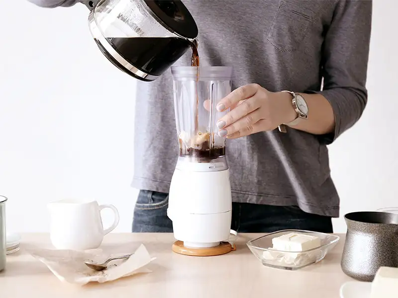 Bulletproof Coffee mit Tasse, Löffeln, Milch und Butter auf Holztisch.